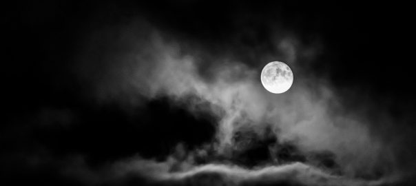 A glowing full moon in a dark cloudy sky.