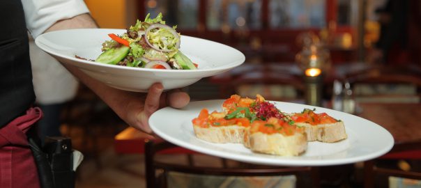 Server holding two meals on white plates.
