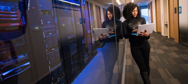 Woman working on a laptop in a server room.
