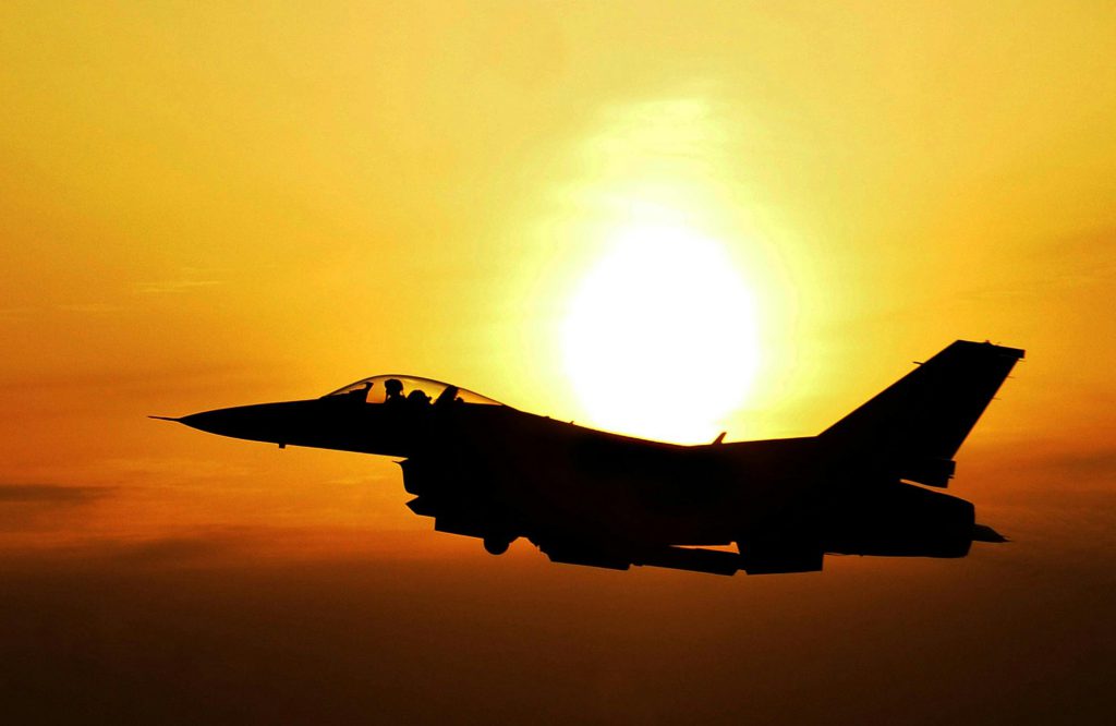 Fighter jet silhouetted against the setting sun.