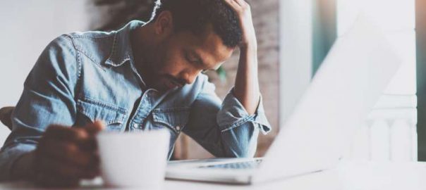 Man in denim shirt clutching his head and looking frustrated.