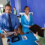 Hispanic Man standing next to African American woman greeting a man holding a professional portfolio.