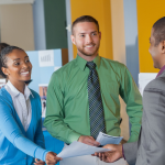 Two students in business attire talk to a prospective employer at a career fair.