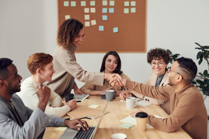 Group of colleagues shaking hands with one another and smiling in a conference room.