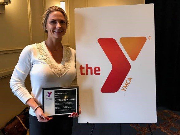 Headshot image of Stephanie Dushane holding 10 year recognition plaque in front of the Ymca sign.