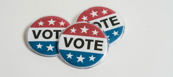 Three red, white and blue pins with the word Vote on them and six white stars are positioned on top of each against a white background.