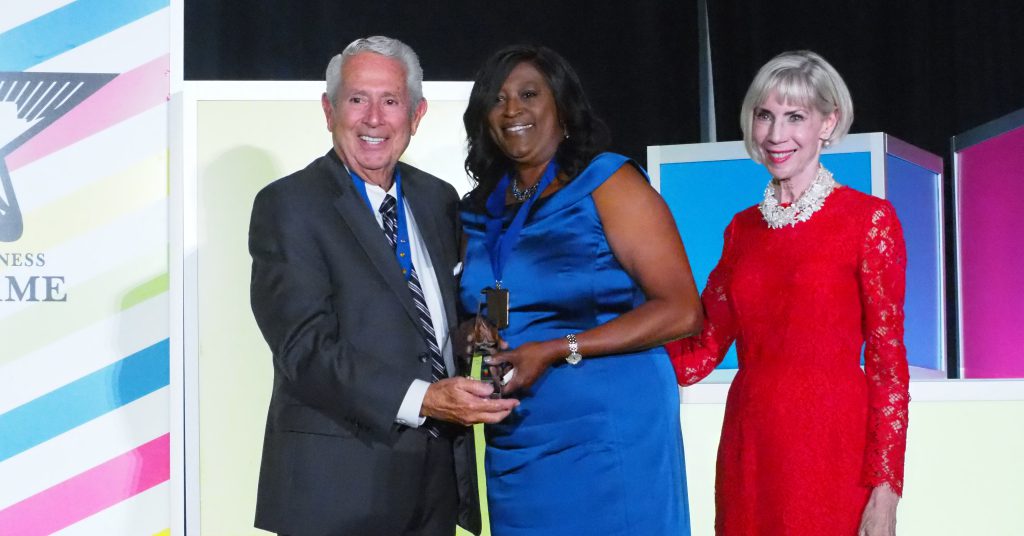Dr. Tonjua Williams accepts her Hall of Fame medal and award on stage while wearing a blue evening gown.