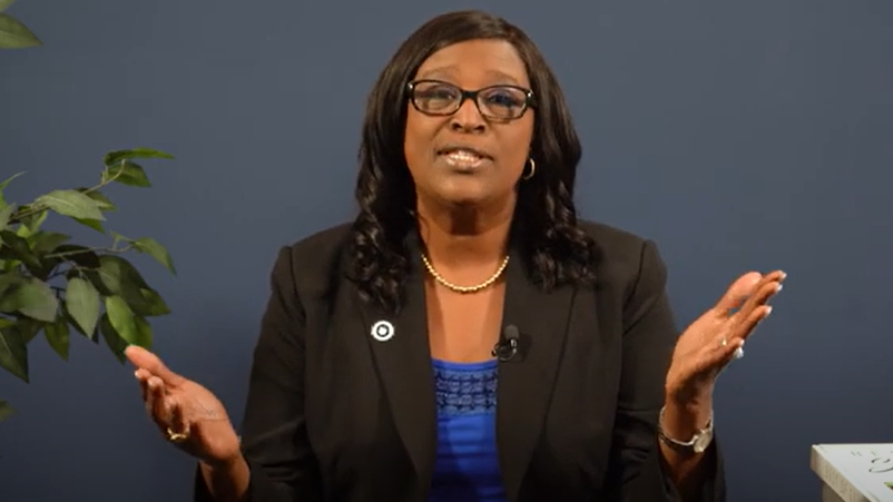 A woman wearing a black and blue suit, holding her hands up.