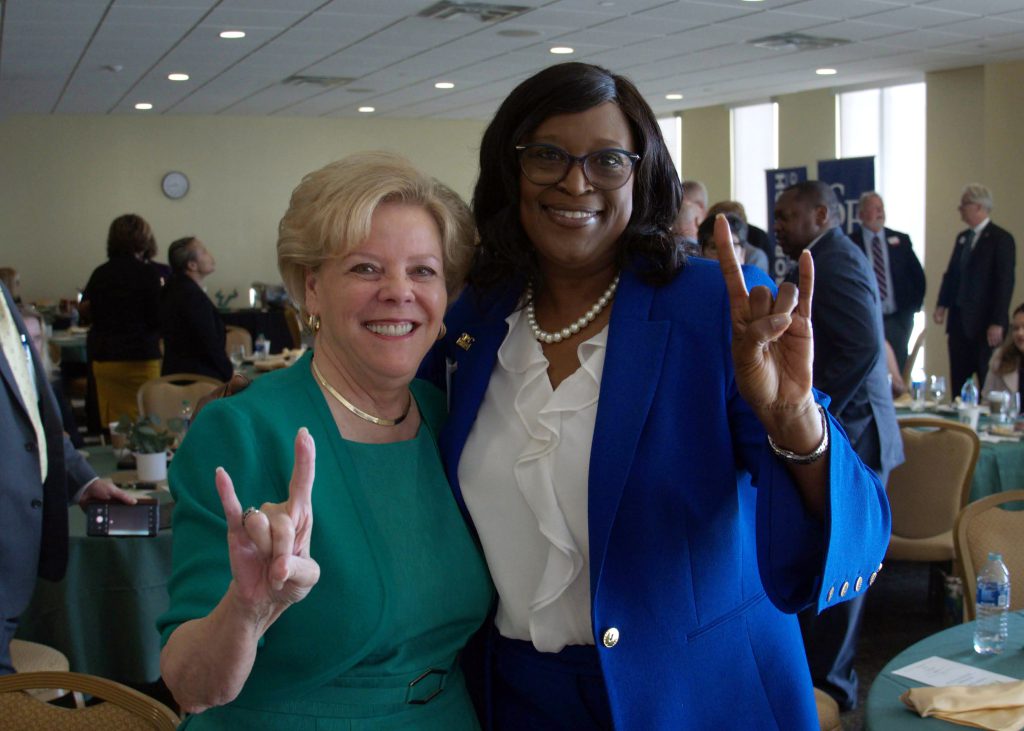 President Williams takes a smiling photo with USF President Rhea Law while they both show the sign for "the horns" with one hand.
