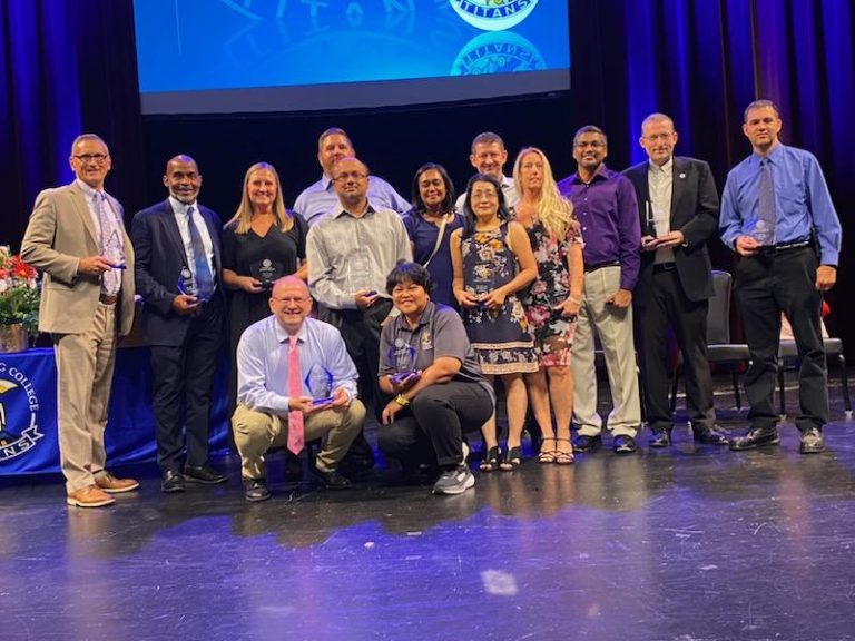 A group of SPC employees, honored at the Fall 2024 Evening of Excellence at the Palladium Theater, stand for a group picture holding their awards.