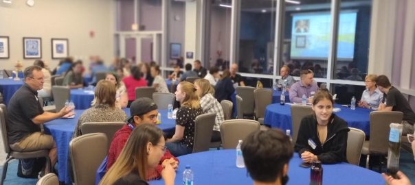 large crowd mingles sitting at round tables