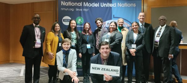 entire team poses with sign that reads "new Zealand", in front of Model UN Banner