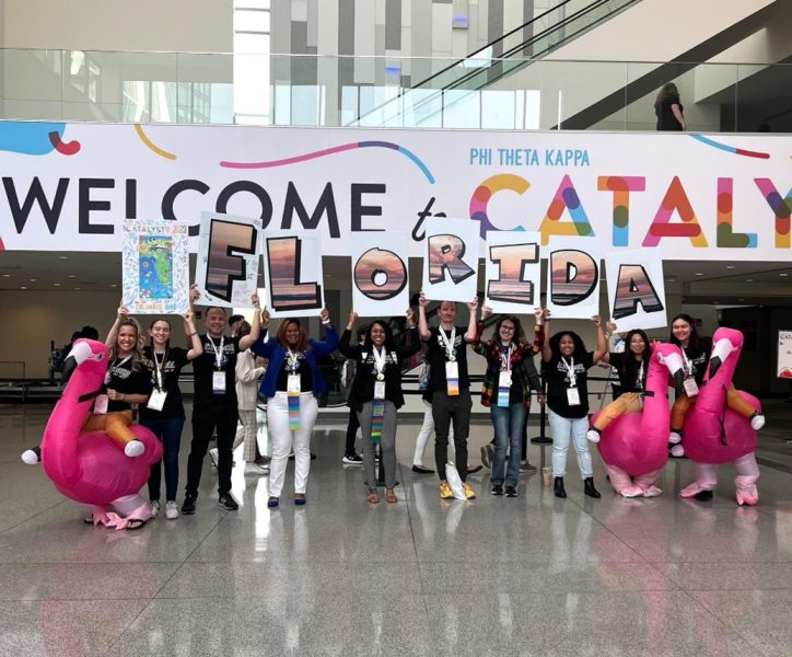 the group stands in front of a sign reading welcome to catalyst. they hold individual letter signs that spell florida